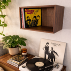 Record player with vinyl records on a wooden console against a wall with a shelf displaying records.