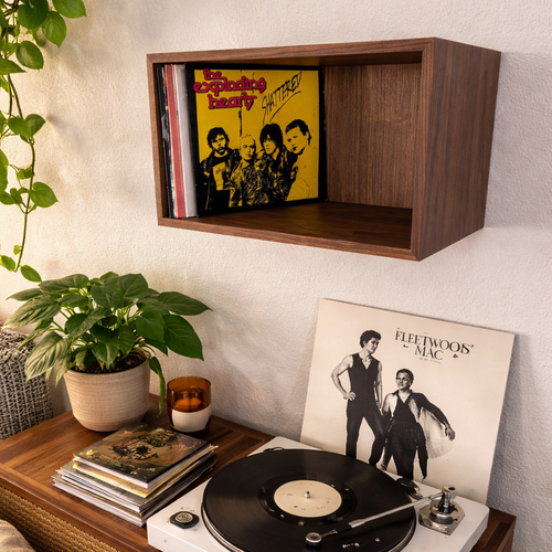 Record player with vinyl records on a wooden console against a wall with a shelf displaying records.